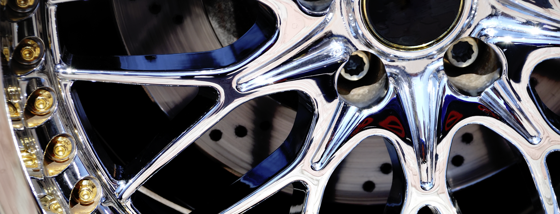 Detailed view of a chrome multi-spoke car wheel with gold bolts and visible brake disc