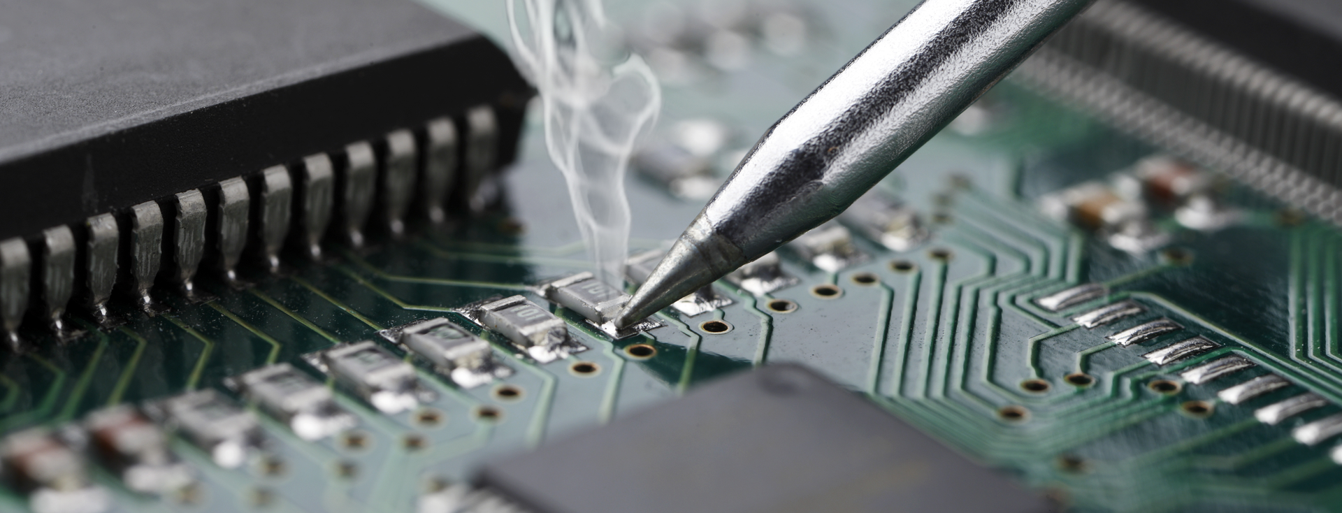 soldering iron soldering a small component onto a green circuit board
